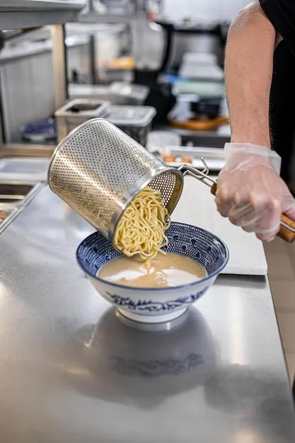 Chef pouring freshly drained noodles into a bowl in the kitchen
