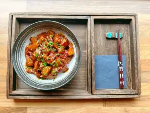 Un plateau en bois élégant avec un plat asiatique aux aubergines. des Baguettes sont disposées sur le coté.